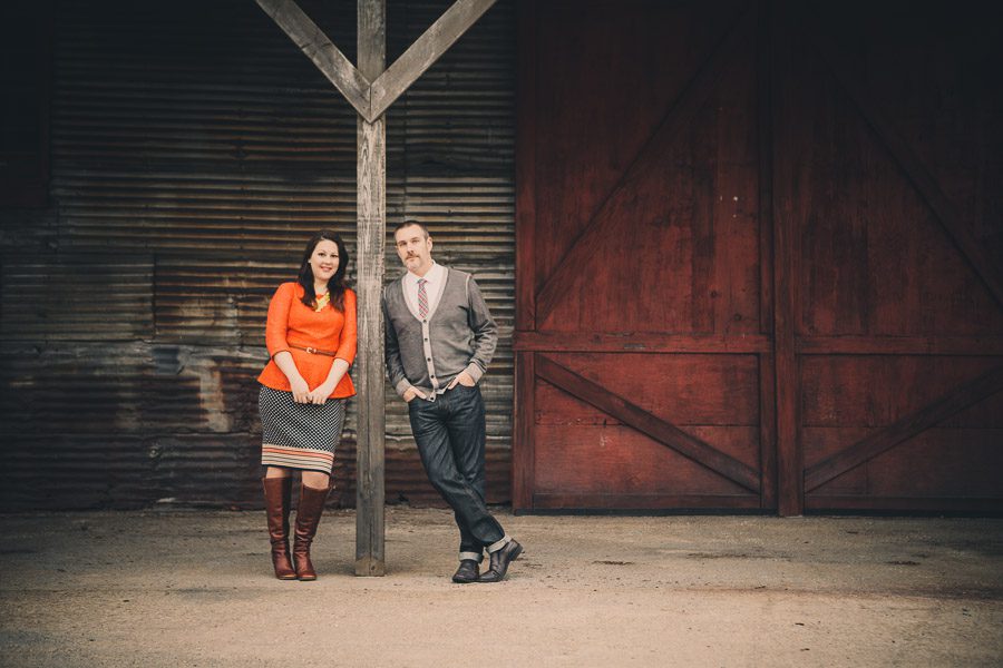 couple leans on post for engagement session at atlanta goat farm