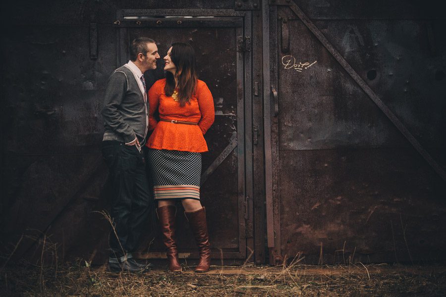 engaged couple kisses in front of grungy doors at goat farm
