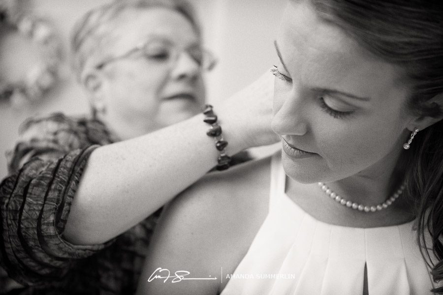 mother helps bride put on necklace