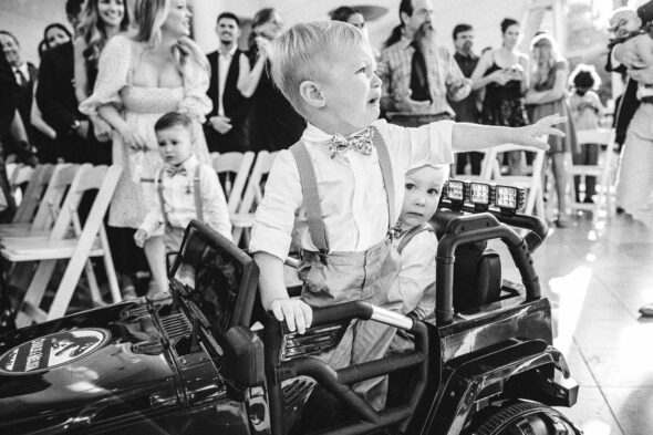 A black-and-white photo of an upset toddler wearing a bowtie during the processional of a wedding ceremony