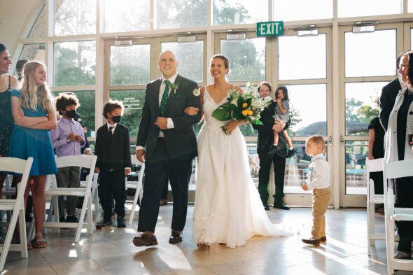Wedding photo of a bride being walked down the aisle by her father at Fern Bank science center