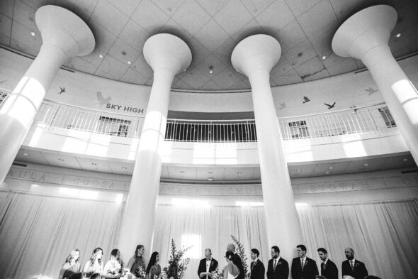 A wide angle black and white view of a wedding with all of the wedding party and the bride and groom at Fern Bank science center