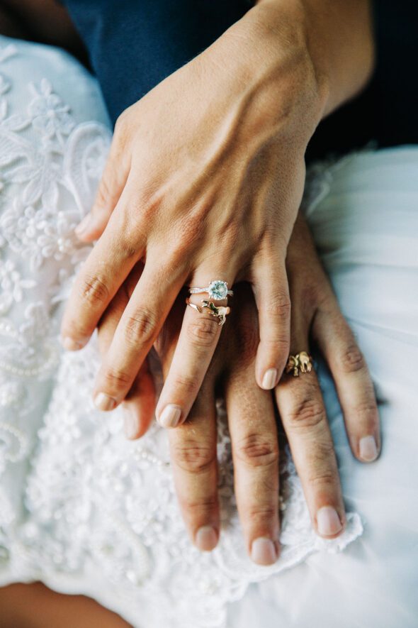 Close up of a man's hand and a woman's hand wearing a dinosaur theme wedding ring