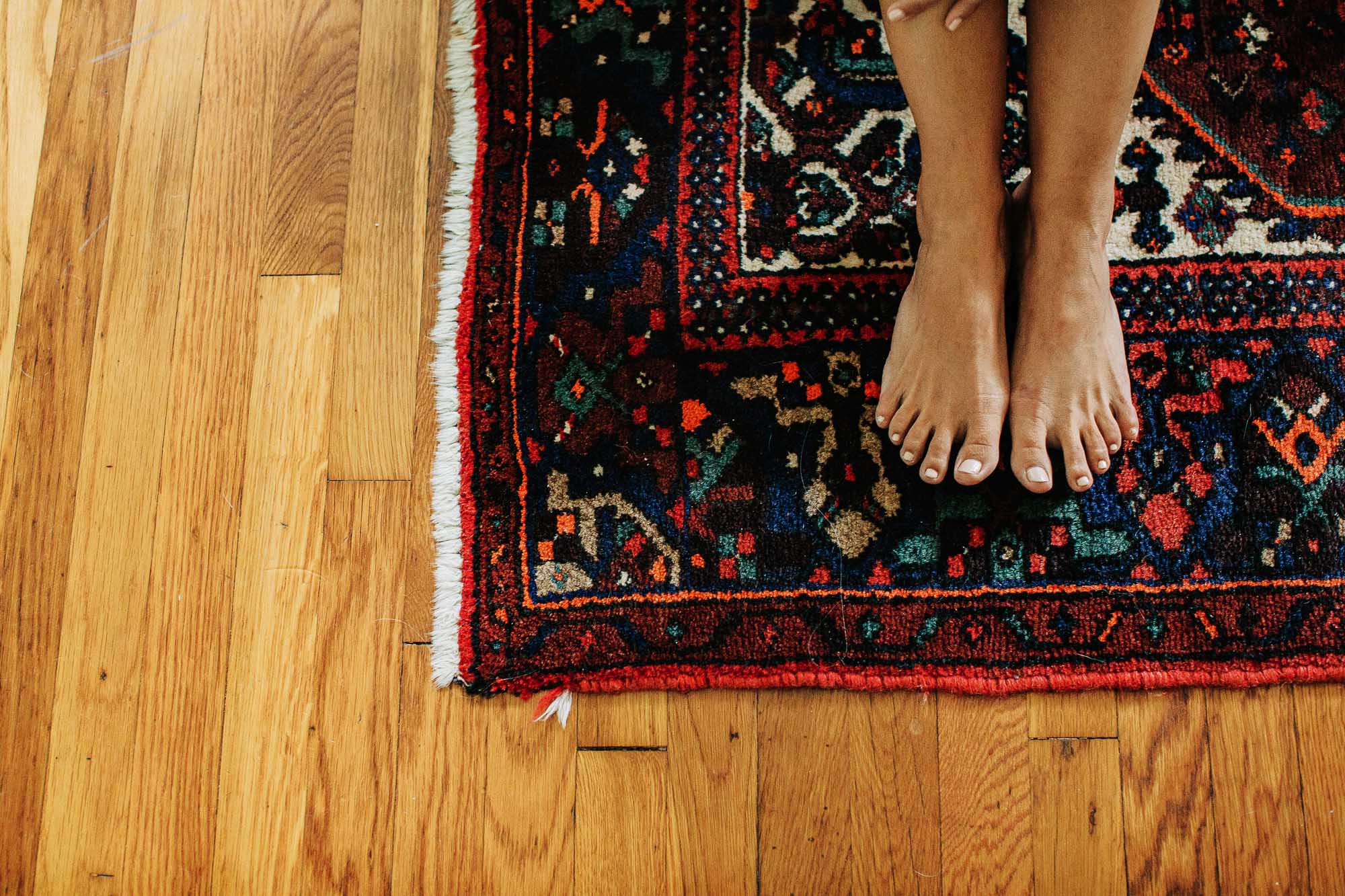 To bare feet on an oriental rug on a hardwood floor