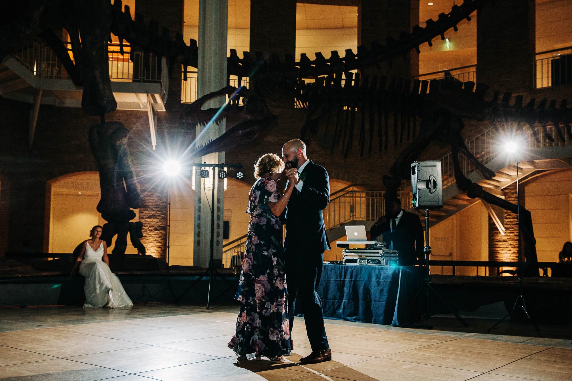 A dramatically lit photo of a groom and his mother having their mother son dance at Fernbank museum