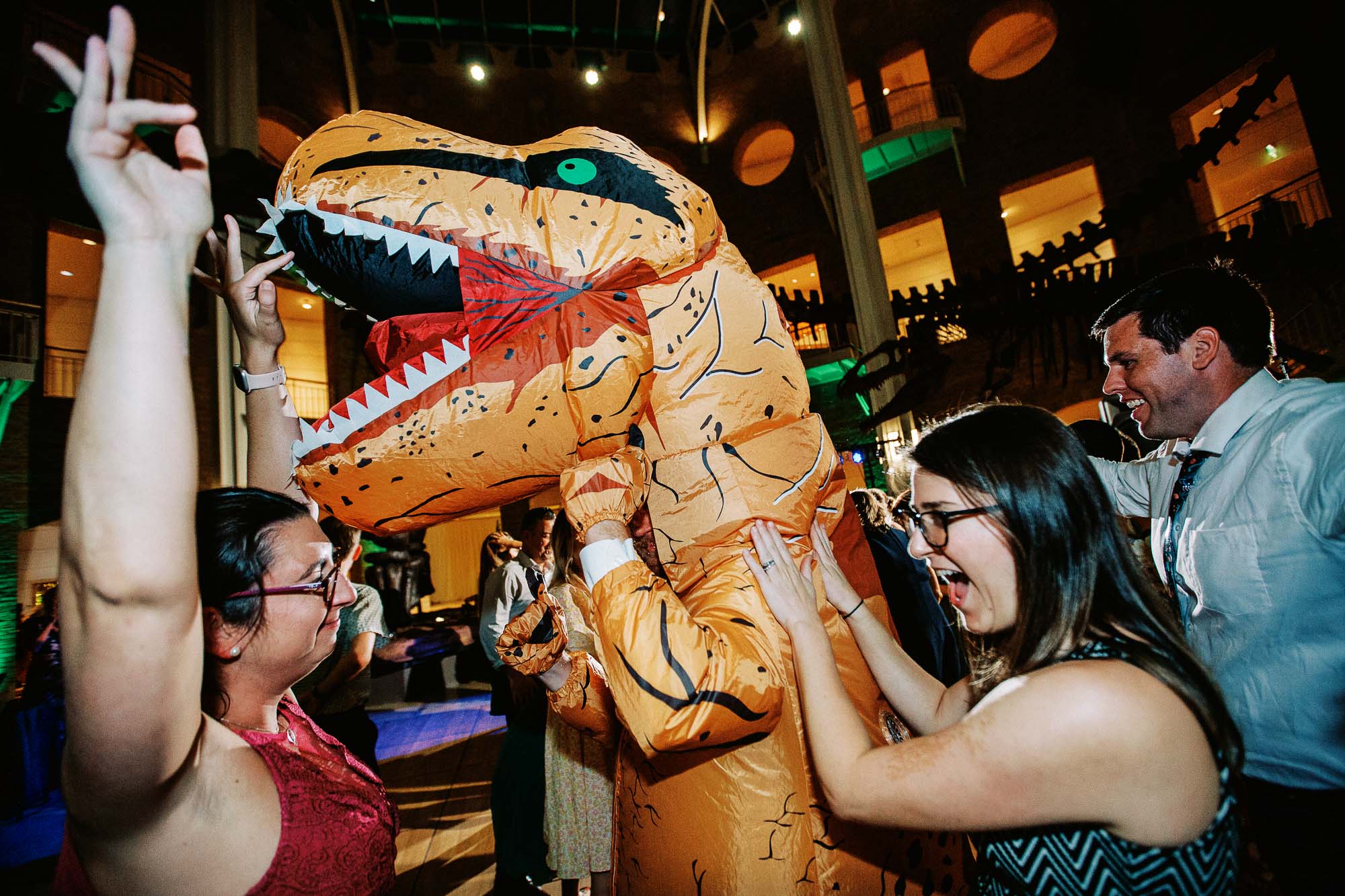A person in a dinosaur costume and two women dance at a wedding