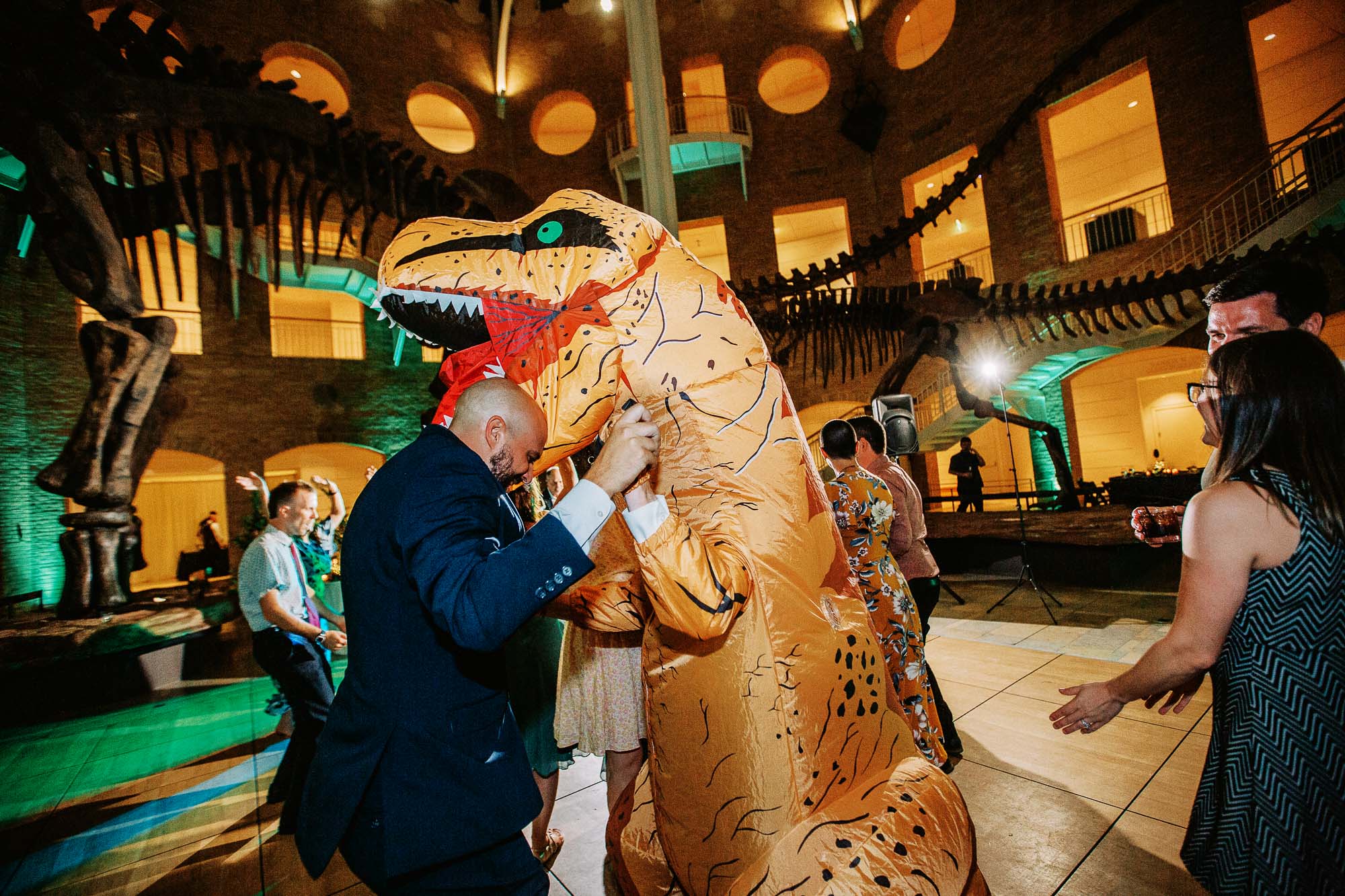 A person in a dinosaur costume dances with the groom at a wedding at Fern Bank museum