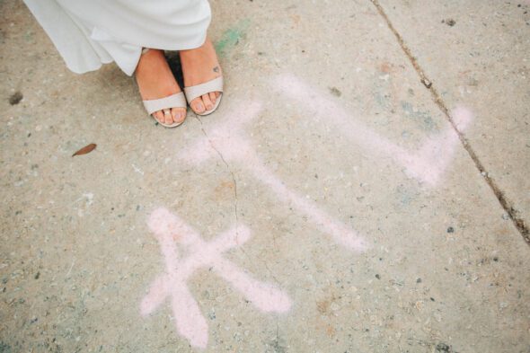 a photo of the feet of a bride wearing a white wedding dress standing next to ATL spray painted on the sidewalk