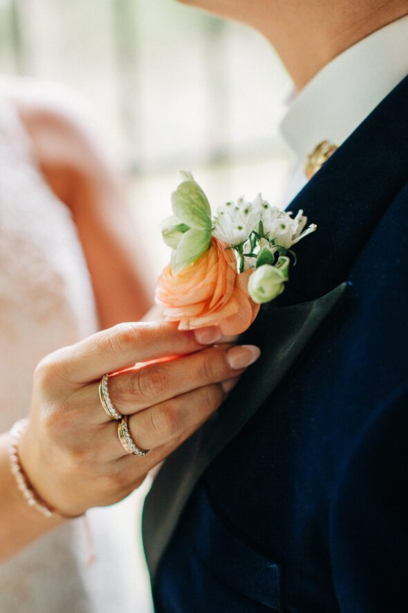 a close up photo of the hand of a bride adjusting the boutonniere of her partner