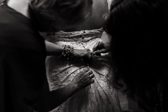 black and white photo of two pairs of hands buttoning the back of a wedding dress