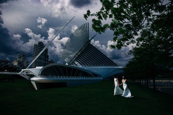 two brides in white wedding dresses walk across the lawn in front of Milwaukee Art Museum