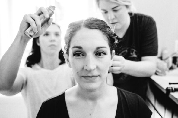 a bride looks off camera while two friends style her hair for her wedding