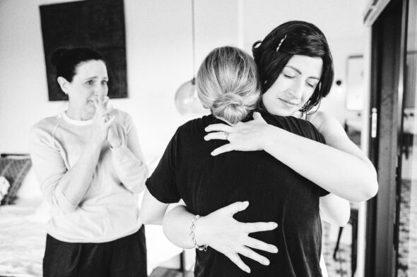 a bride hugs her sister while their mother looks on in tears