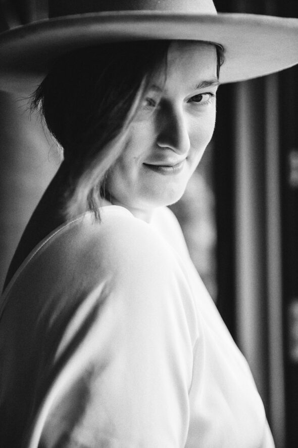 black and white photo of a bride wearing a hat looking over her shoulder at the camera