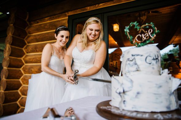 two brides wearing white wedding dresses cut their wedding cake with a sword