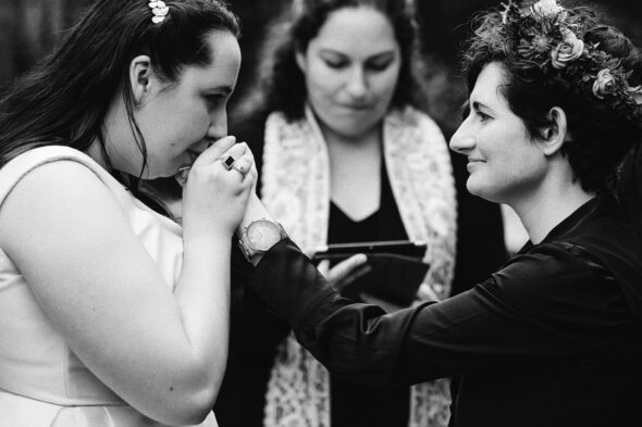 a bride kisses the hand of her nonbinary partner during their wedding ceremony
