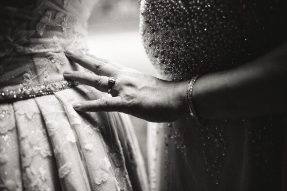 black and white photo of two brides standing close together with one brides hand touching the dress of the other bride