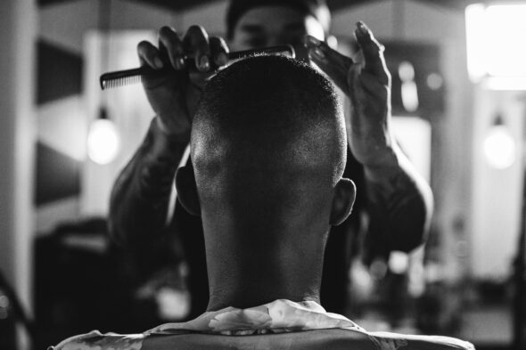 black and white photo of the head of a groom from behind having his hair styled by a barber