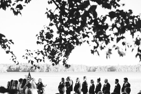 black and white photo of a wedding ceremony by a lake from under a tree branch
