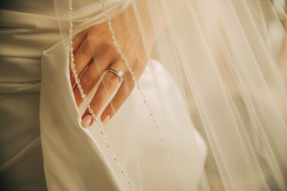 photo of a bride's hand under her veil holding her wedding dress