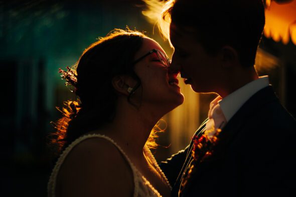 an LGBTQ couple kiss on their wedding day lit by the setting sun