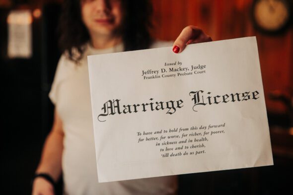 a groom with a red manicure holds up a marriage license