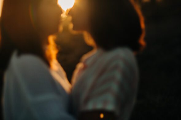 out of focus engagement photo of couple facing each other in the sunlight at sunset