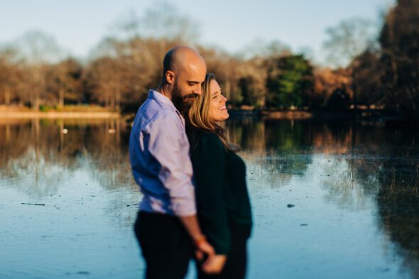 a couple stands close and hold hands on the pier at Piedmont park in Atlanta for their engagement photos