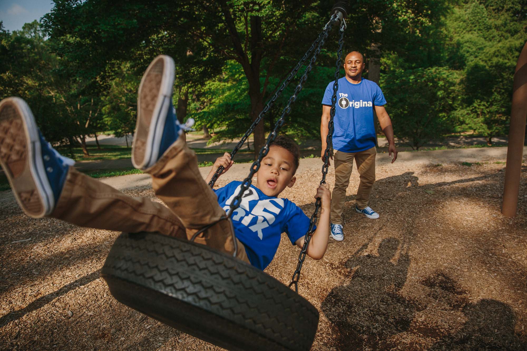 a Black father pushes his son on a swing in an Atlanta park