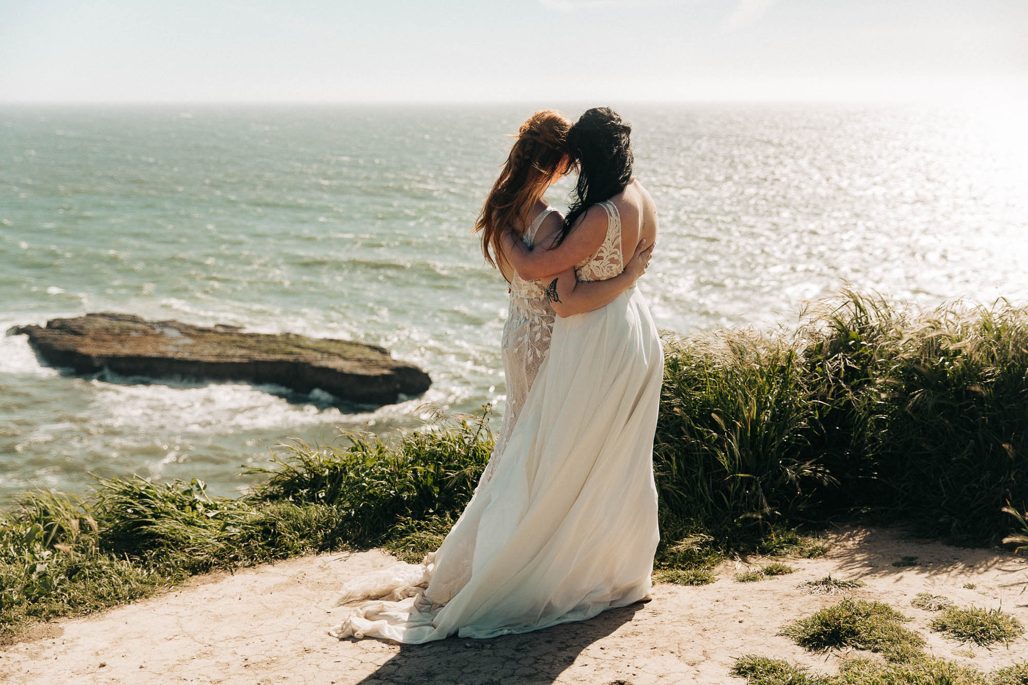 newlywed lesbian couple stands looking at the ocean on the coast of California
