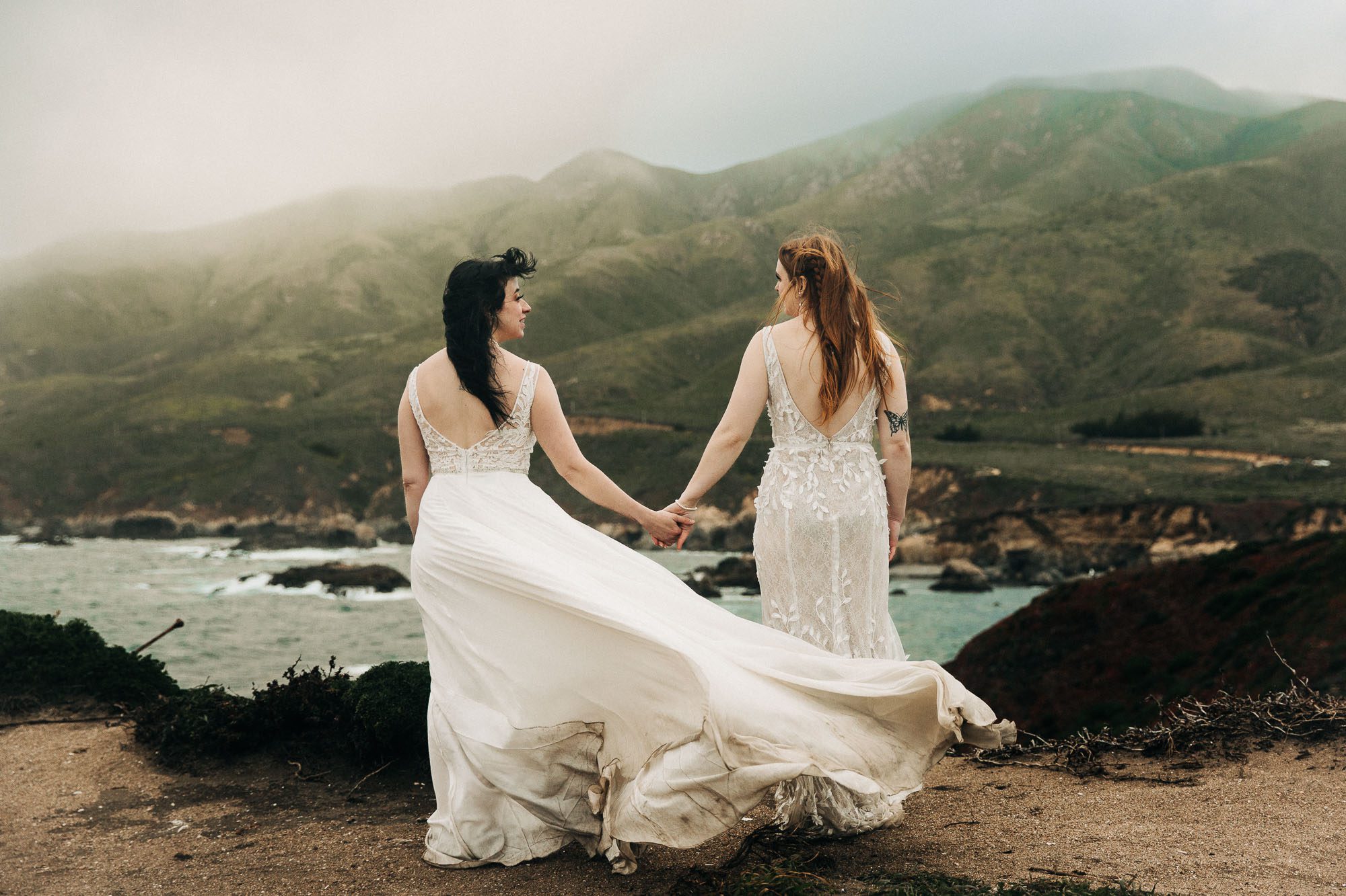a newlywed lgbtq couple stands on the cliffs overlooking the ocean in Big Sur