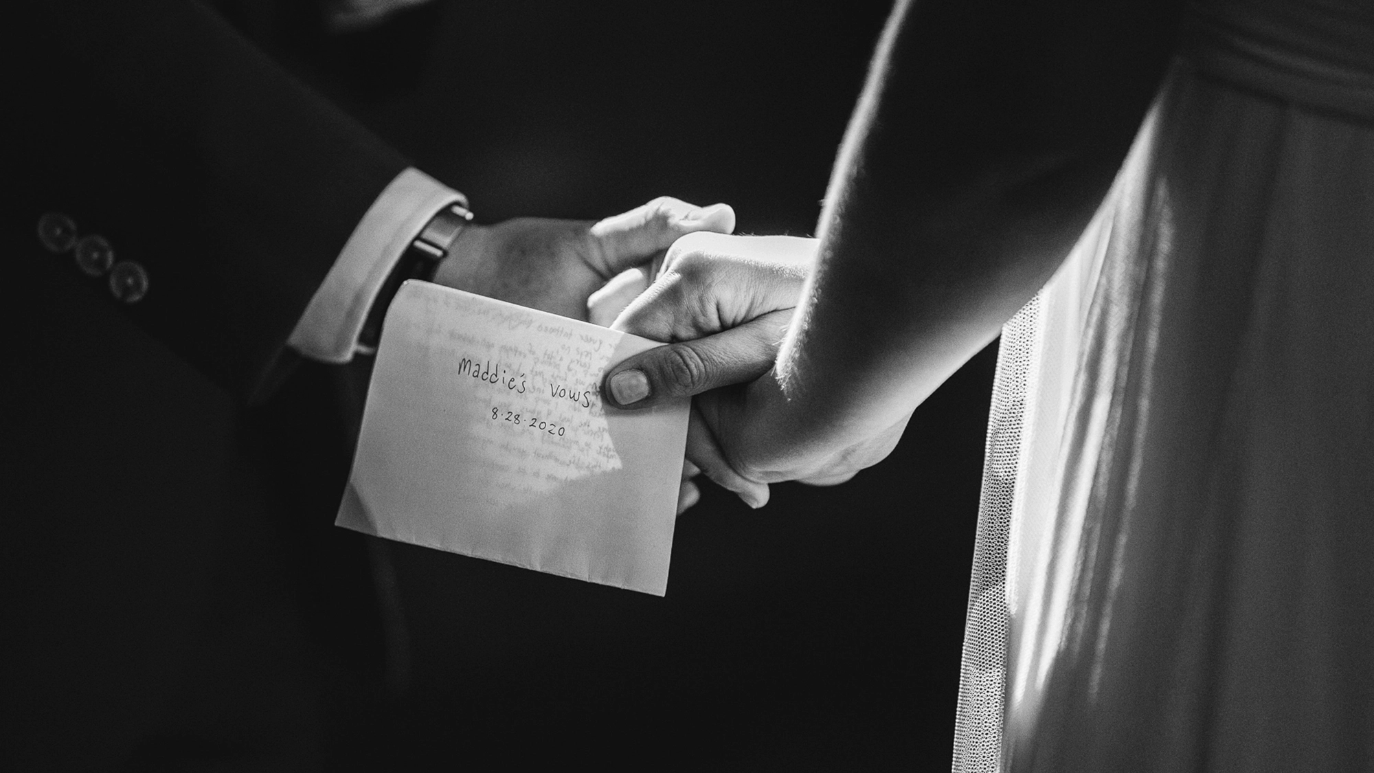A couple holds hands at their wedding, one of them holding their vows in a folded piece of paper.
