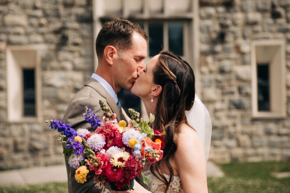 a bride and a groom kiss behind the wedding bouquet