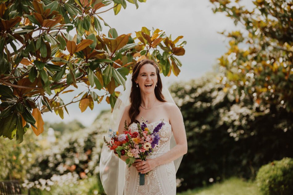 a bride stands in front of a magnolia tree laughing happily