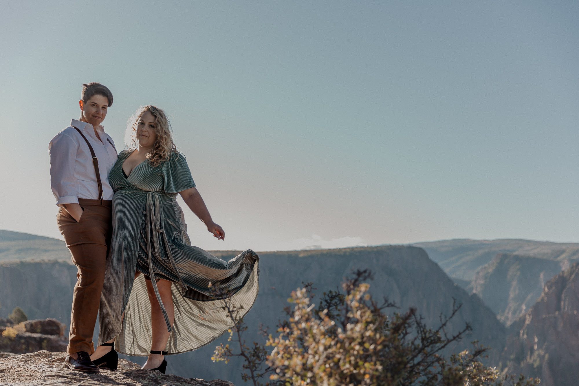 LGBTQ couple stands on the rim of a canyon for their adventure engagement photos