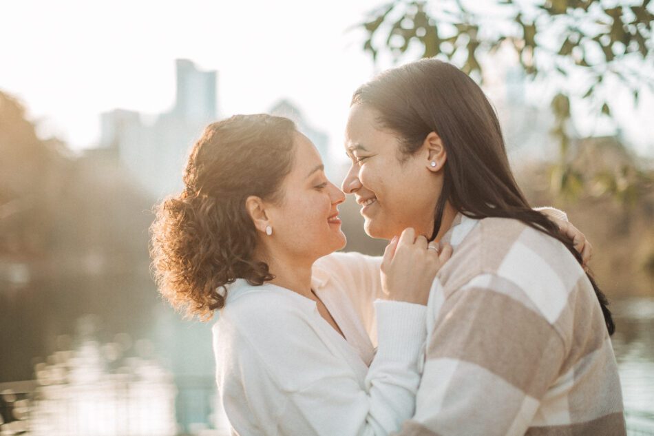 two smiling women embrace and lean in close for a kiss in front of the lake at Piedmont Park in Atlanta