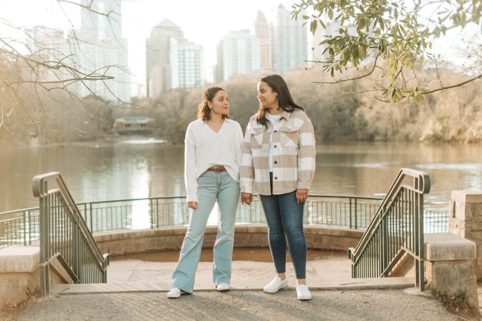 an lgbtq couple holds hands in front of the lake at Piedmont Park with the Atlanta skyline behind them during their engagement photo session