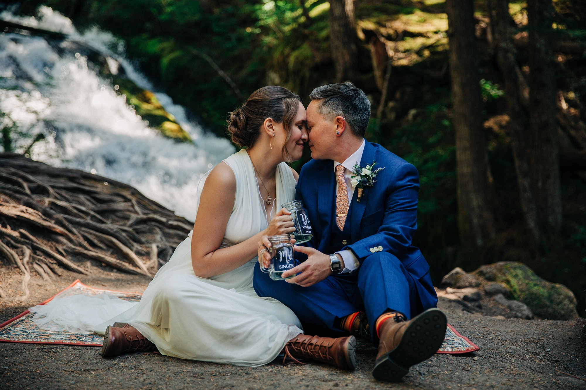 a bride and her nonbinary partner share a kiss at a waterfall in Mt Hood NF on their wedding day