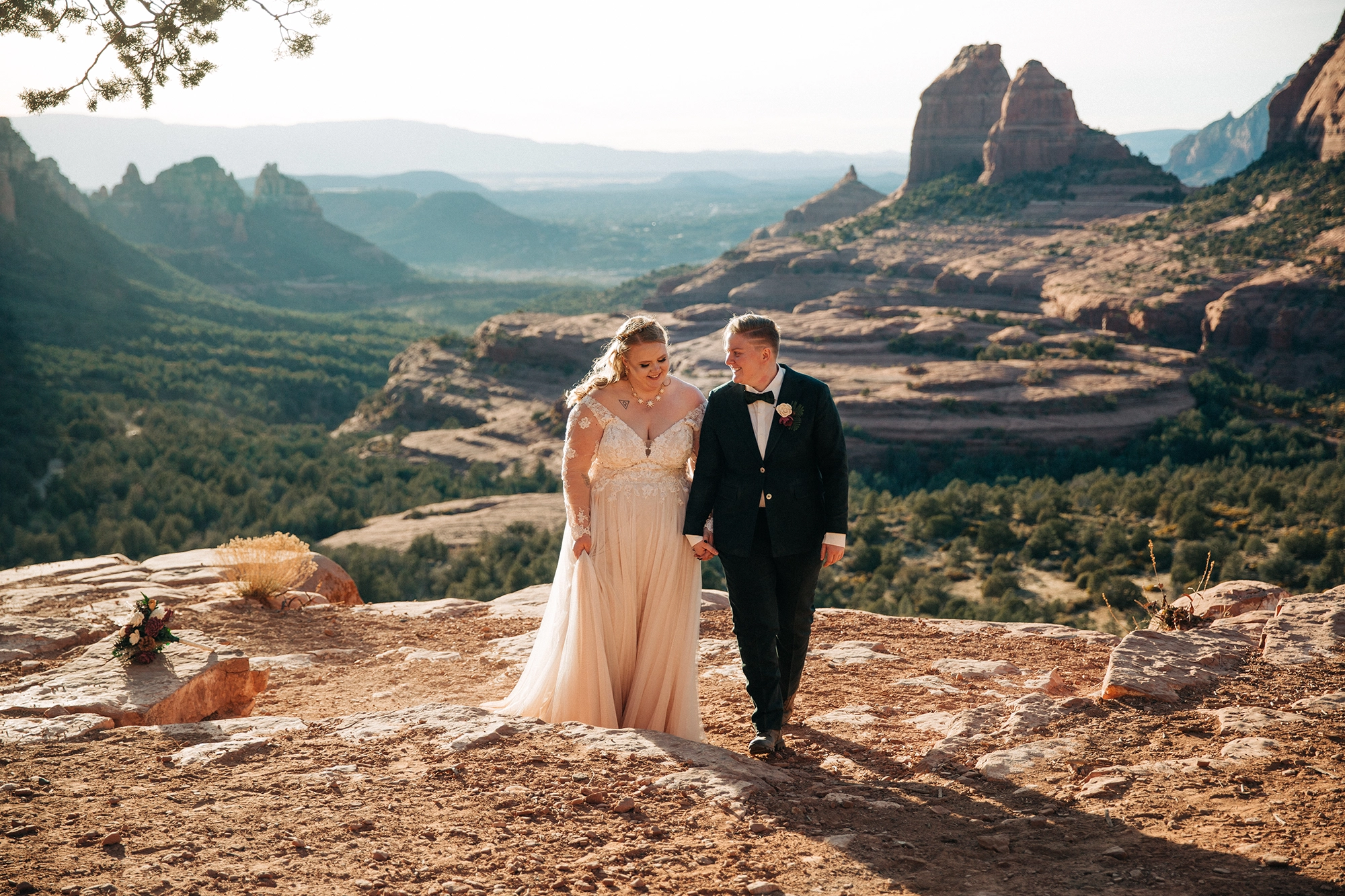a lesbian couple walk hand in hand along a cliff in Sedona after their elopement wedding ceremony