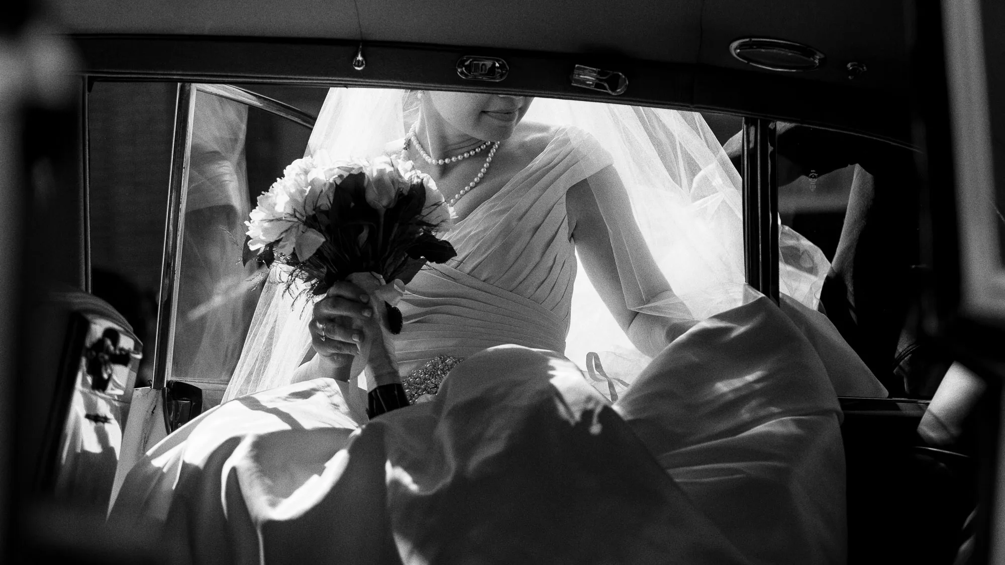 a bride wearing a white wedding dress and long veil holds her bouquet carefully as she enters the back seat of a vintage car on her wedding day in a photo by Atlanta wedding photographer Amanda Summerlin