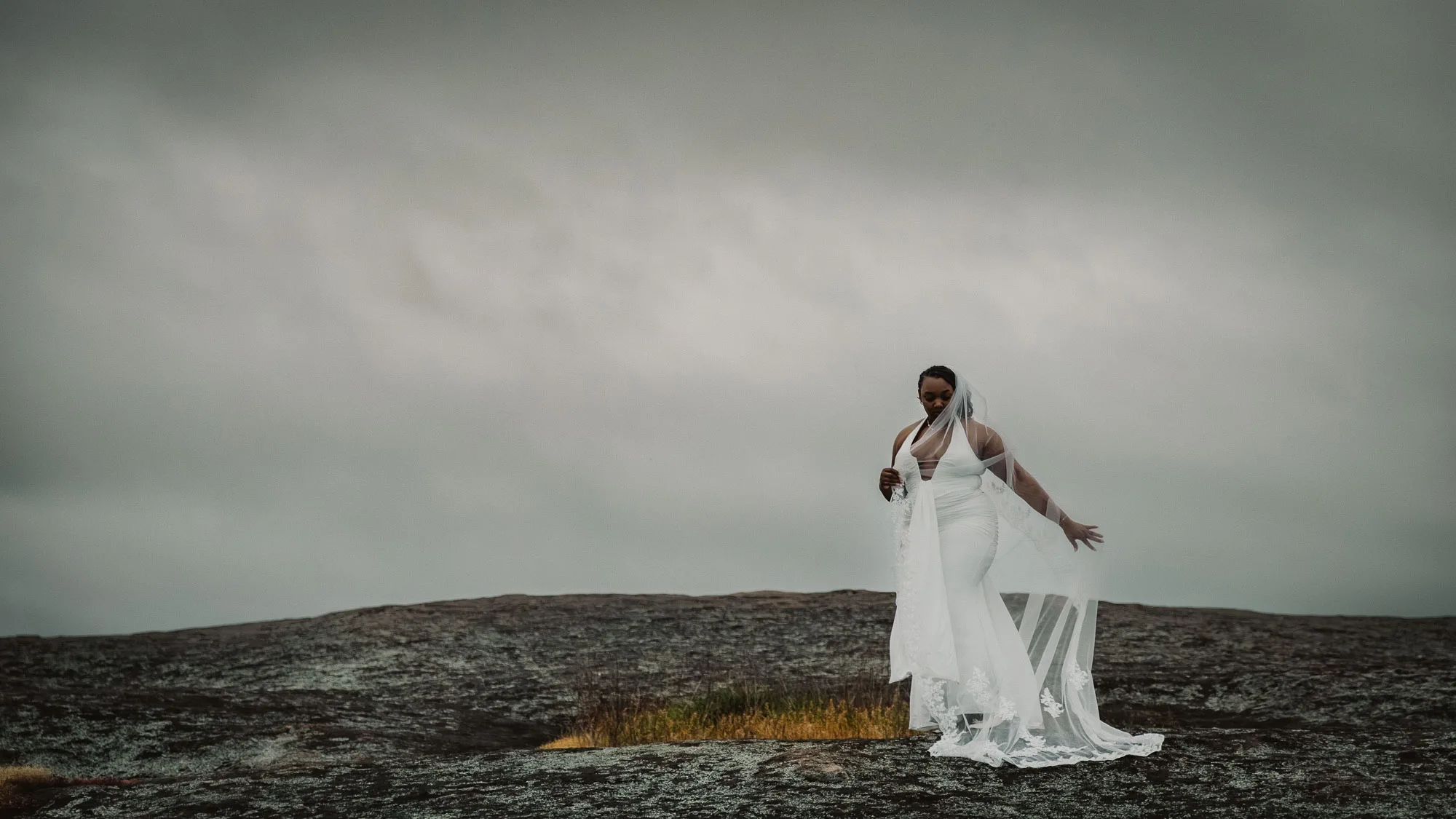 a black bride in a white wedding gown stands at the top of arabia mountain at sunrise on a cloudy day adjusting her veil