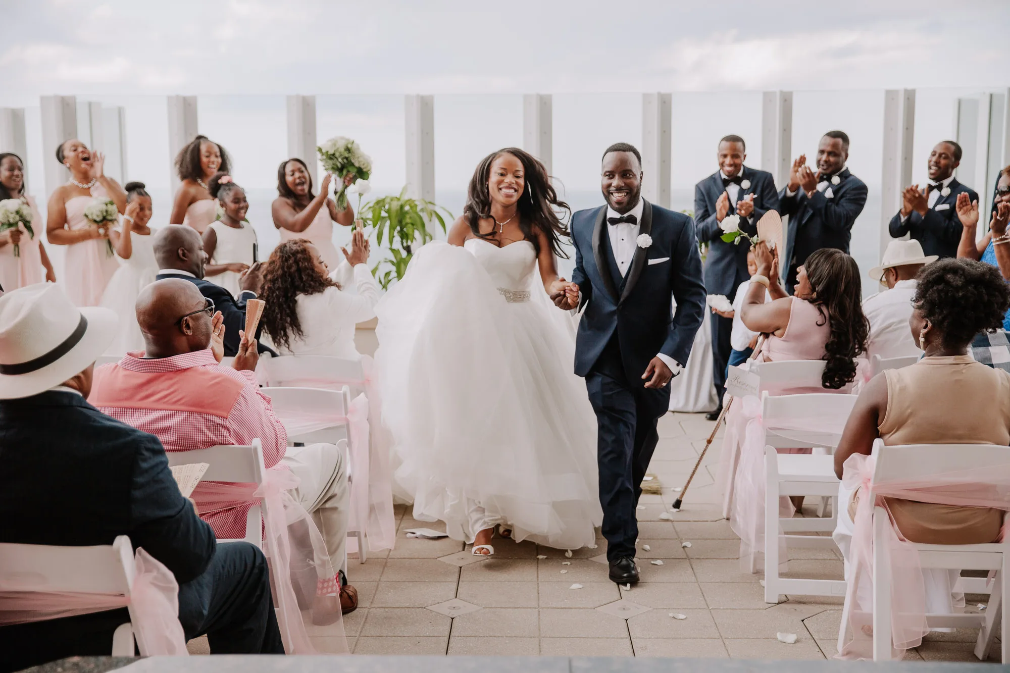 A Black bride and groom holding hands and walking down the aisle after their ceremony with joyful, giant smiles at an Atlanta wedding