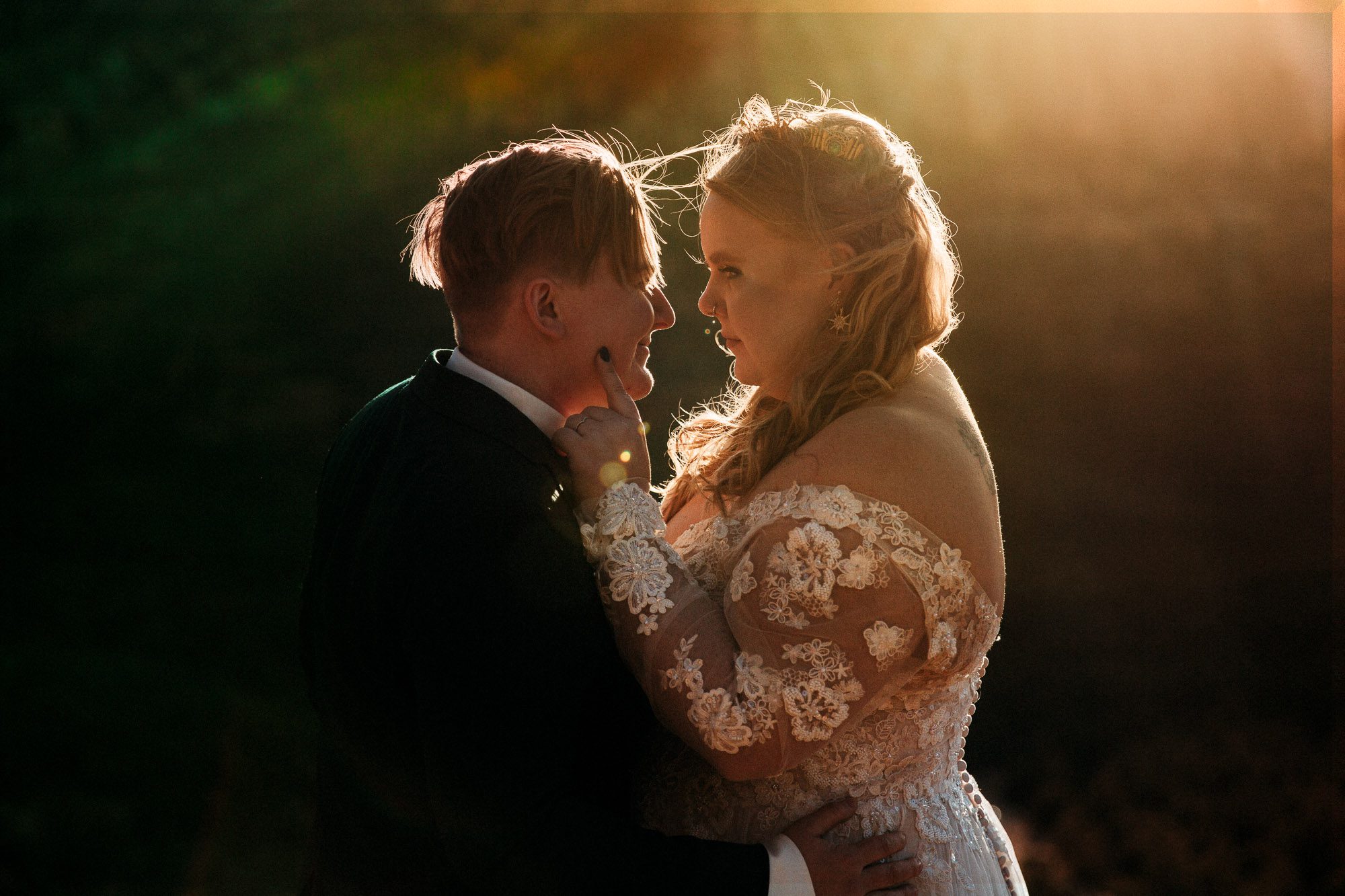 an lgbtq couple faces each other in an embrace in front of a sunset on their wedding day