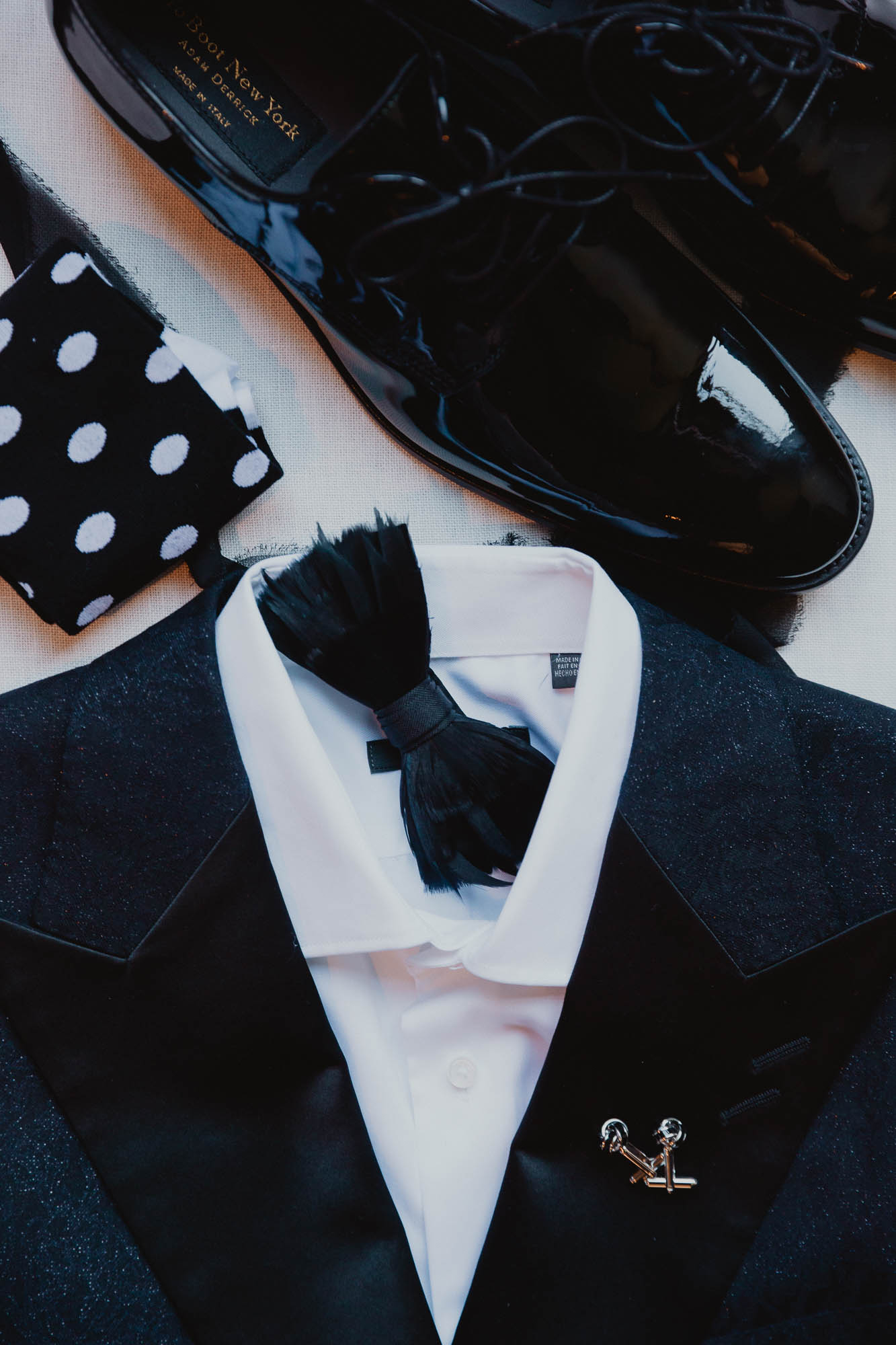 flat lay photo of a black suit with a black bowtie and black patent leather shoes