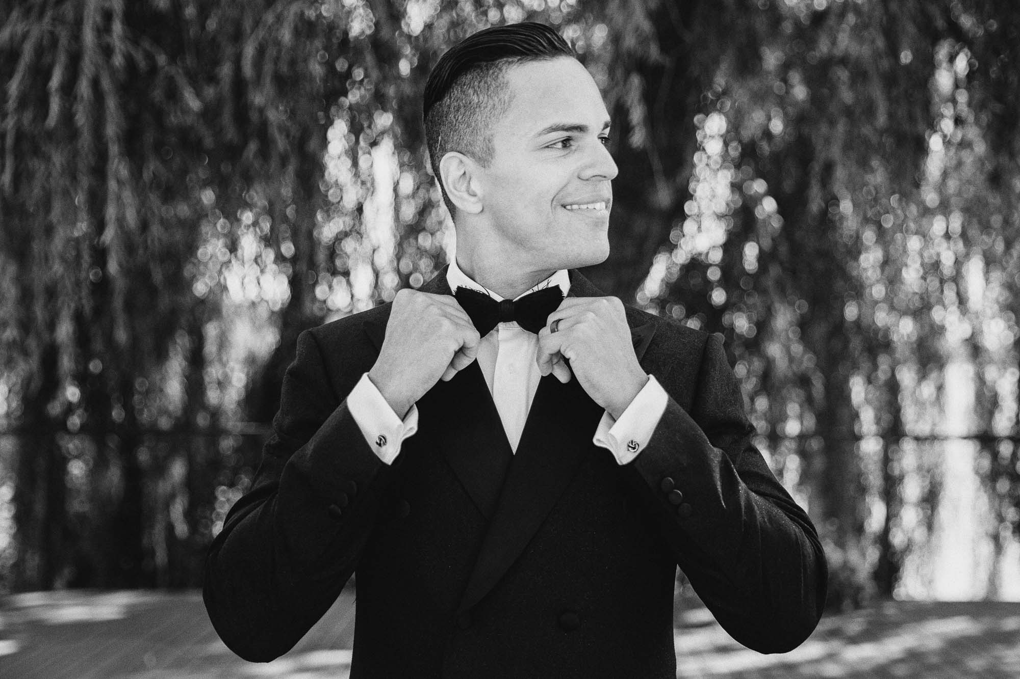 an lgbtq groom in a black suit straightens his bowtie