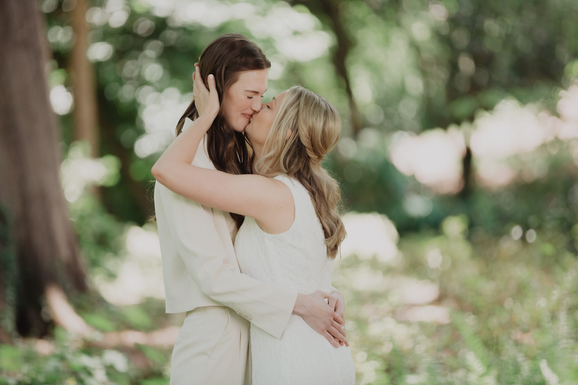 Two brides wearing white kiss during an emotional first look at Cator Woolford Gardens in Atlanta just before their wedding ceremony