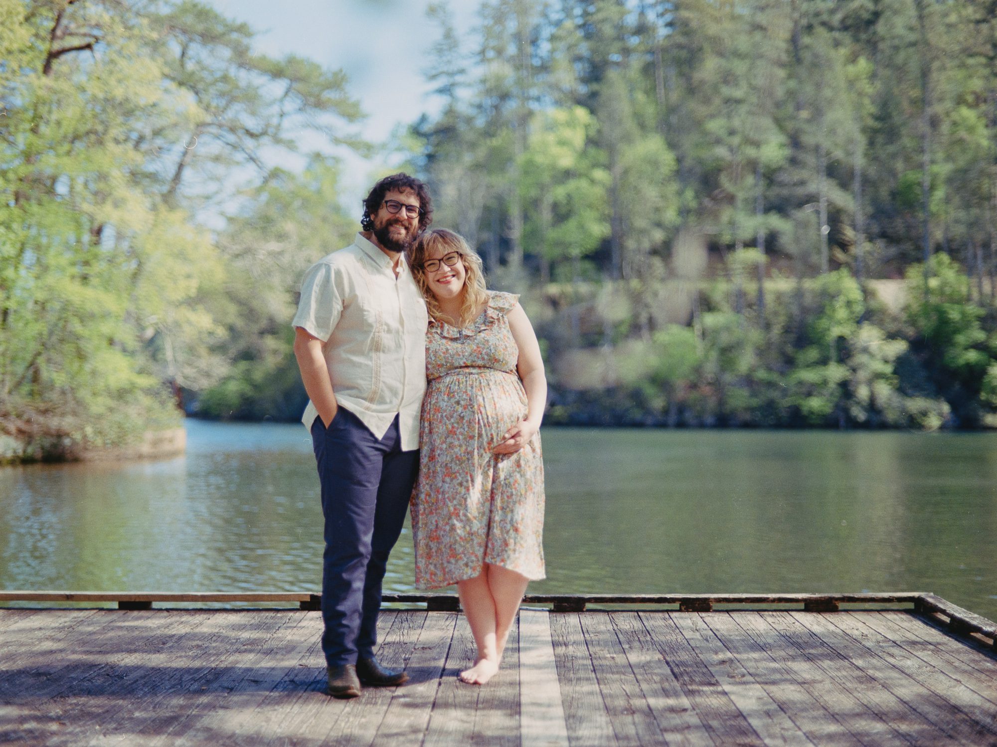 a man and a woman stand in the afternoon sunshine on a dock on Lake Rabun for their maternity photos