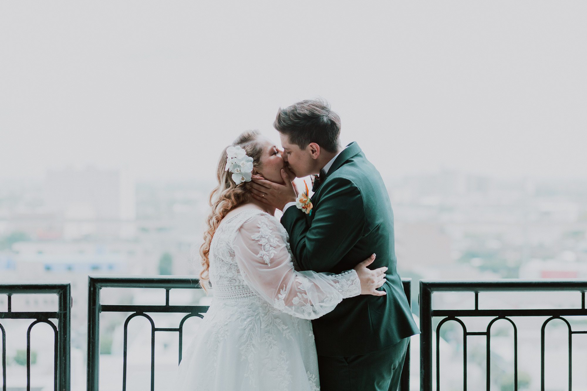 a bride wearing a white dress kisses her nonbinary spouse wearing a green suit on their wedding day