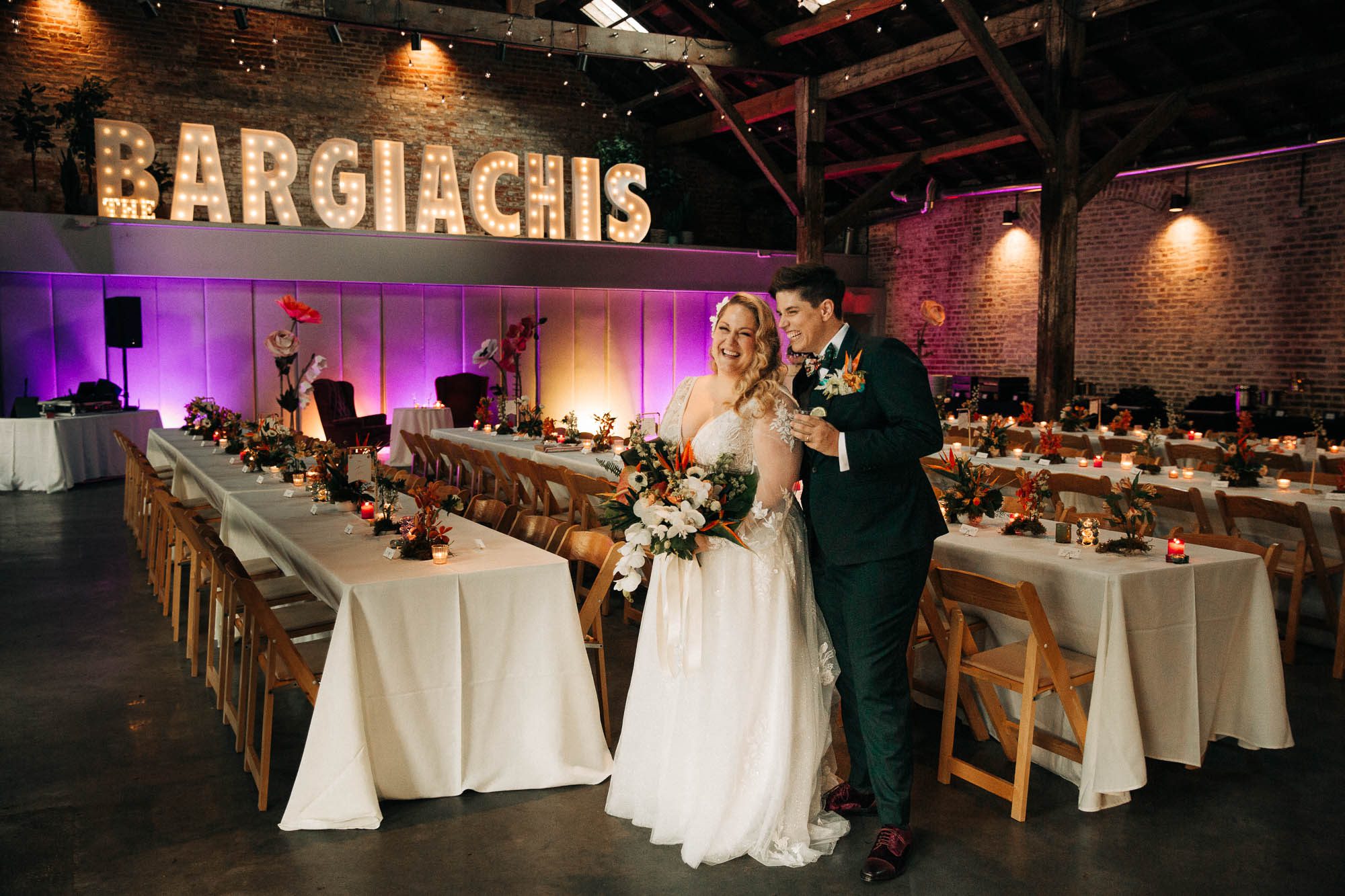 a queer couple stands laughing in their beautifully decorated wedding reception at Capulet in New Orleans
