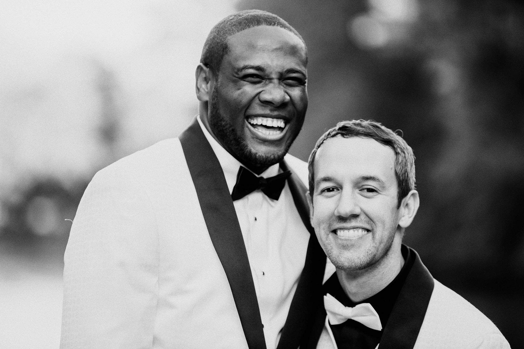 Wedding portraits in historic Atlanta Piedmont Park, LGBTQ male couple in wedding attire embrace while one man laughs.